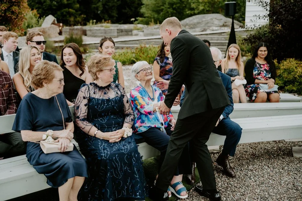 Will greeting an older guest as family wait on white benches before the ceremony at Le Belvedere