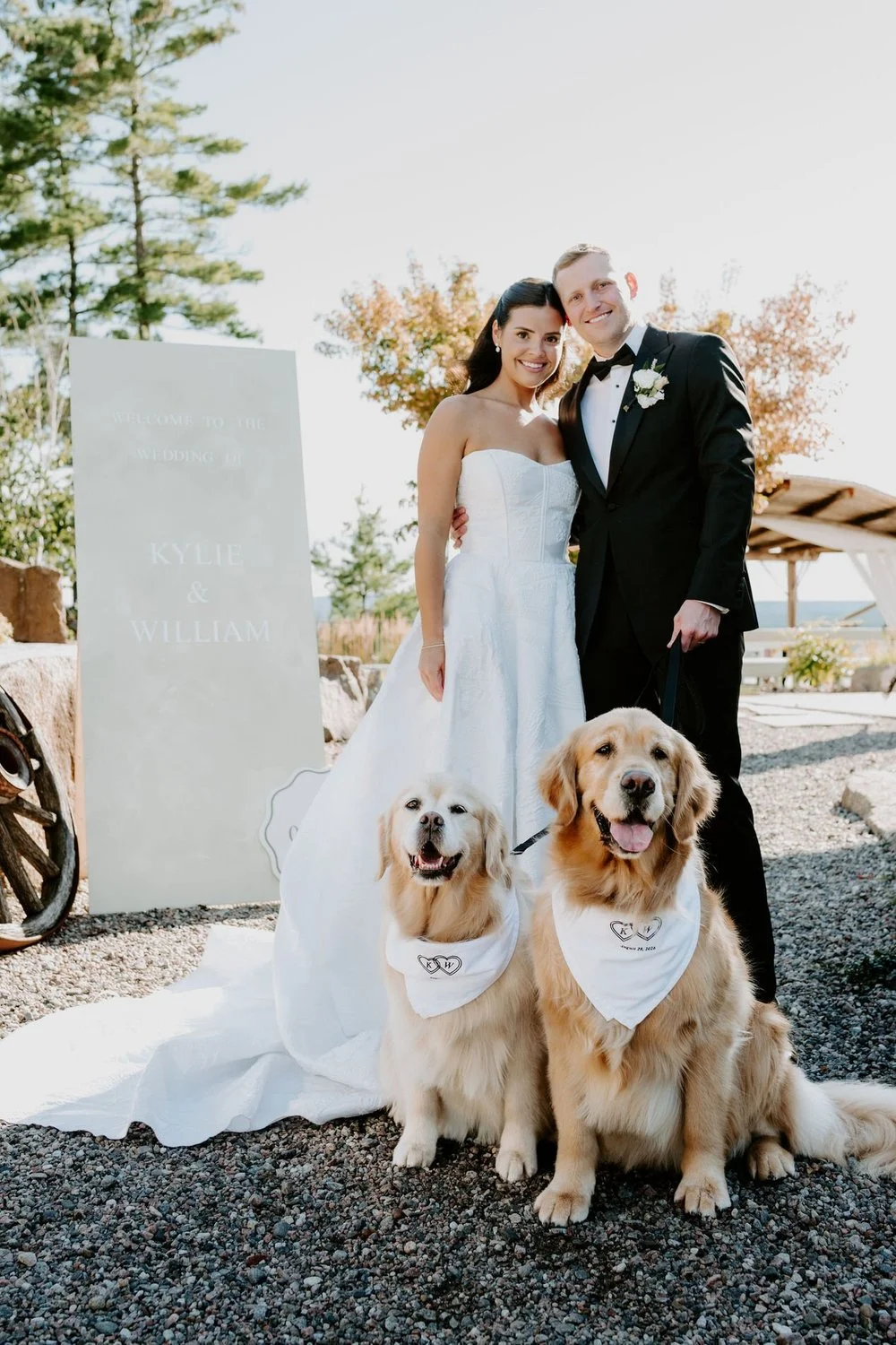 Kylie and Will with their two golden retrievers beside a "Kylie & William" welcome sign at Le Belvedere