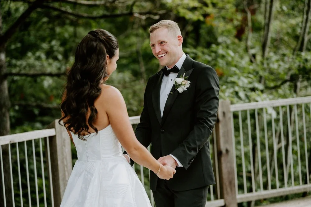 Kylie and Will holding hands during their first look on a wooden deck surrounded by trees at Le Belvedere