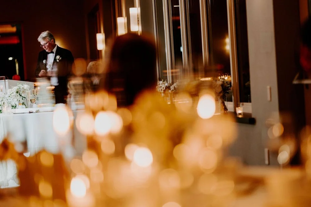 An older man in a tuxedo giving a speech, seen through glowing candlelight
