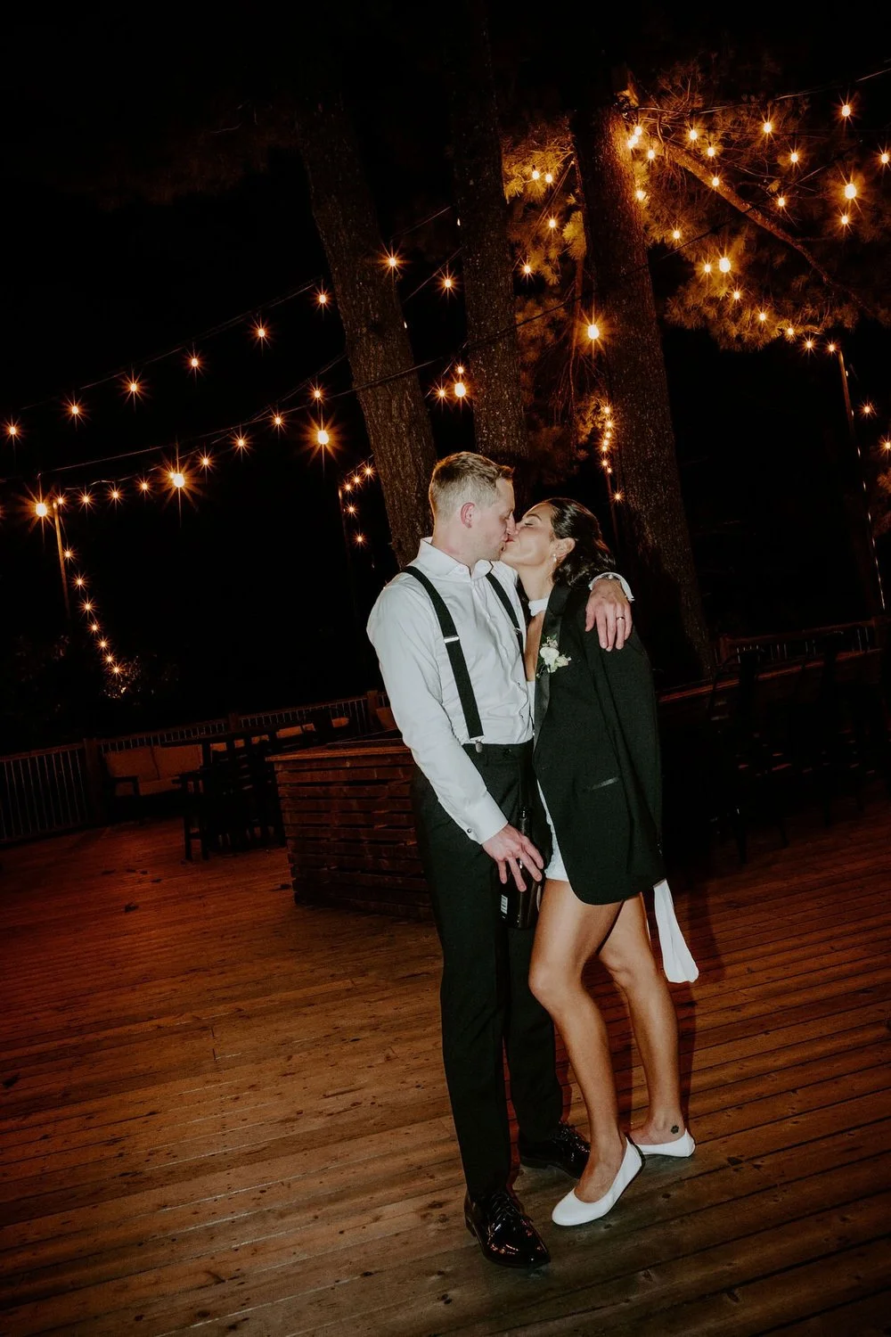 Kylie and Will kissing under string lights on the deck at Le Belvedere at the end of the night