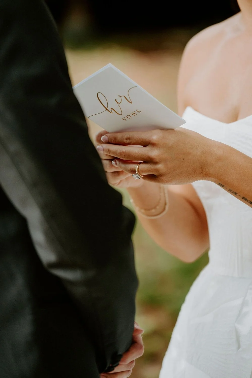 Close-up of Kylie holding a card reading "her vows" in gold script