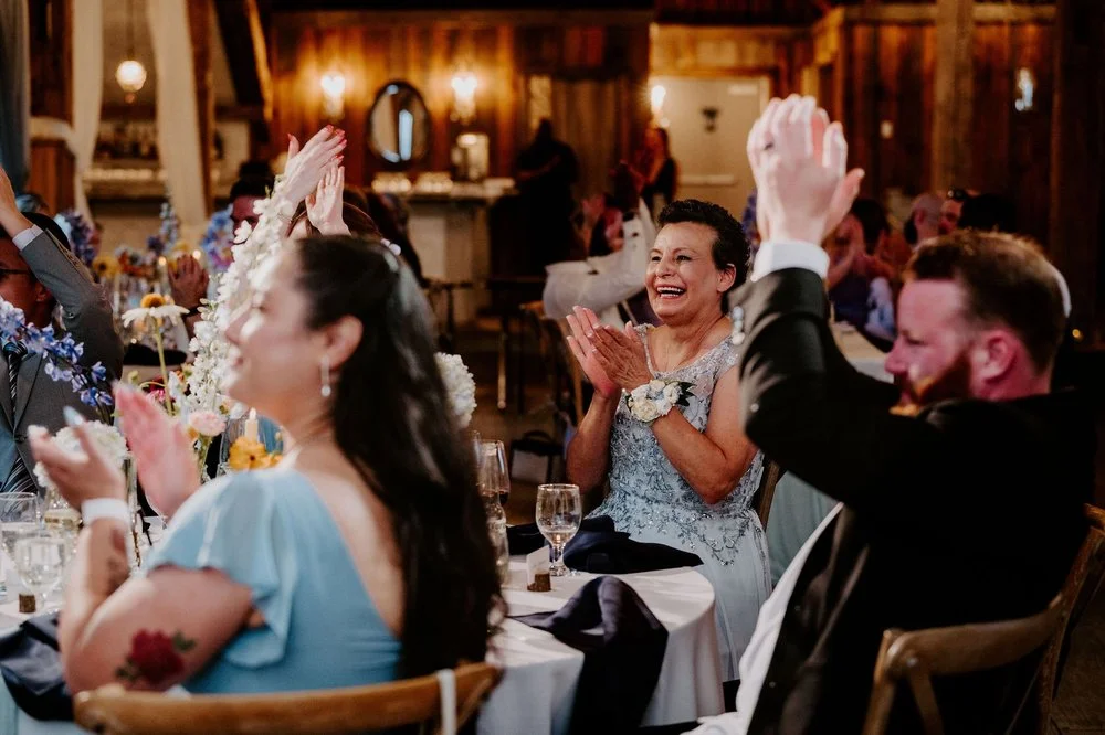 Guests applauding at Holly and Petar's reception, a woman in a blue lace dress beaming