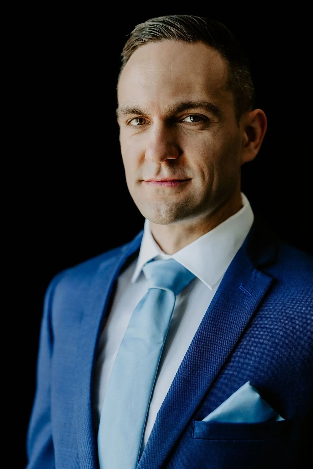 Portrait of the groom, Petar, in a blue suit, pale blue tie and pocket square against a dark background