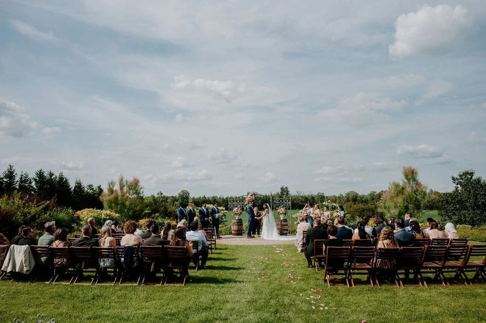 Wide view of Holly and Petar's outdoor ceremony on the lawn at Evermore in Ottawa, under a big cloudy sky