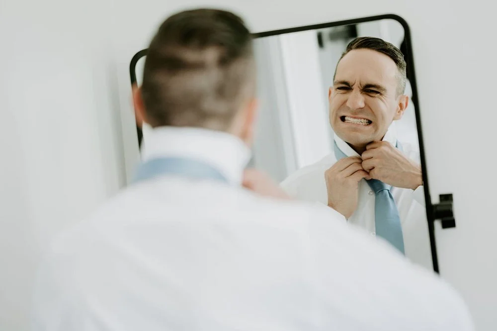 Petar pulling a playful grimace in the mirror while tightening his pale blue tie