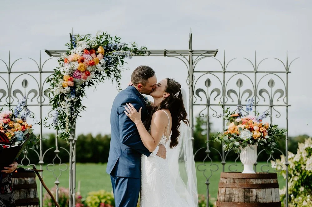Holly and Petar's first kiss under the flower-covered wrought-iron arch at Evermore in Ottawa