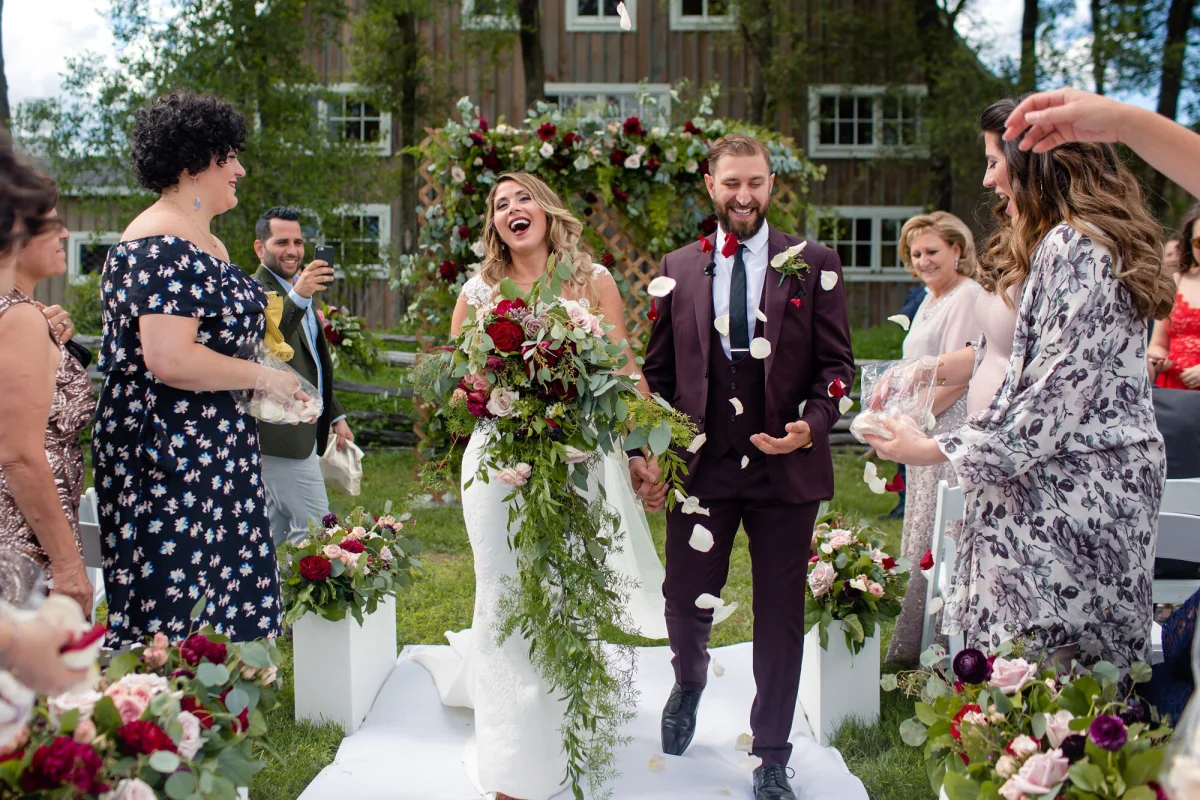 Smiling bride and groom being showered with flower petals while walking down the aisle after outdoor wedding ceremony at Stonefields Estate