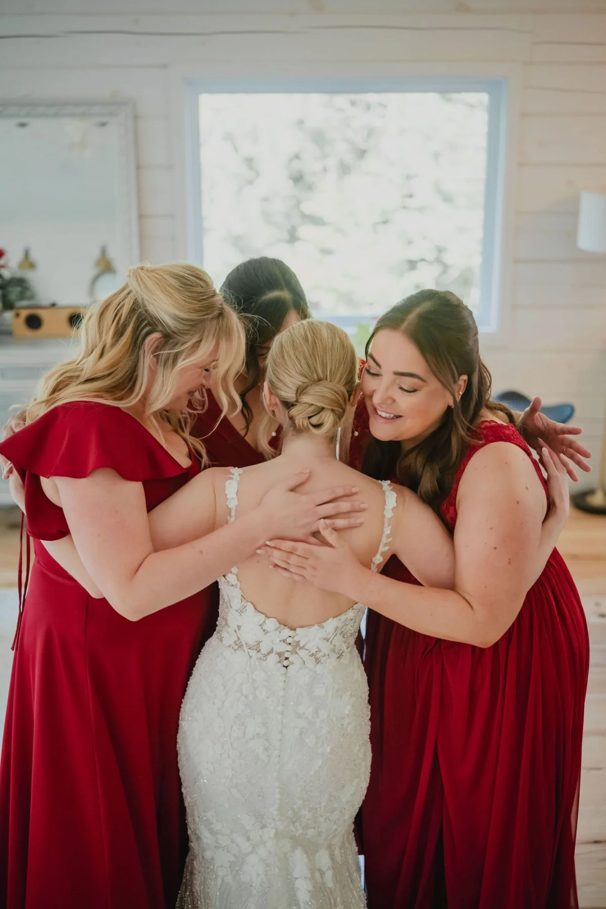 bridesmaids hugging the bride after she gets into her wedding dress