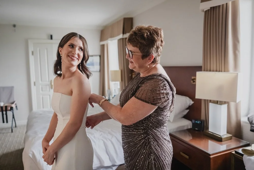 a mother helps her daughter get into her wedding dress