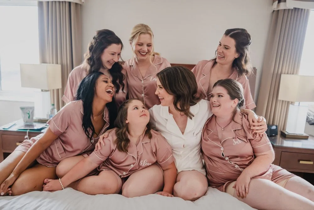 bridal party getting ready for a wedding in pink gowns on a bed