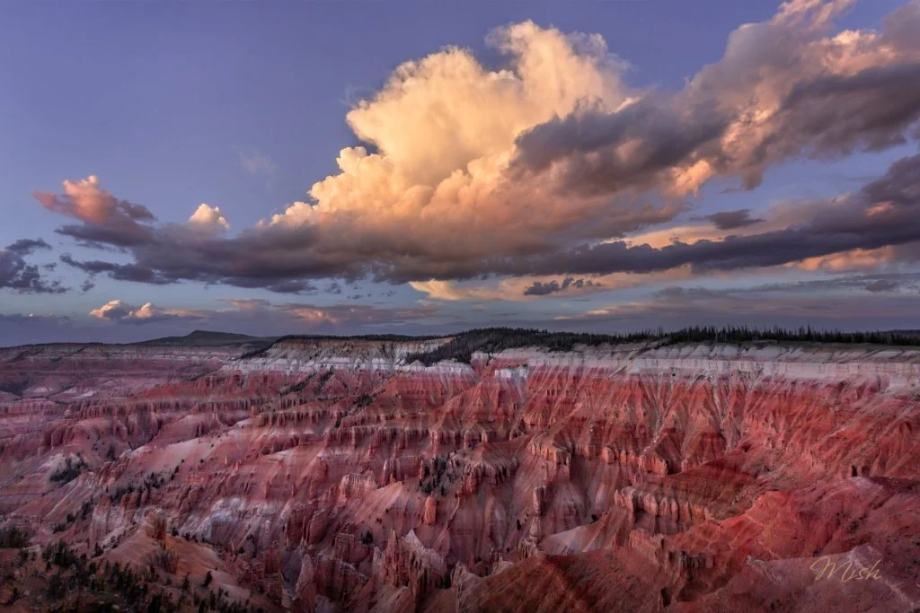 A panoramic view of a colorful canyon landscape at sunrise, featuring layered red and white rock formations under a cloudy sky.