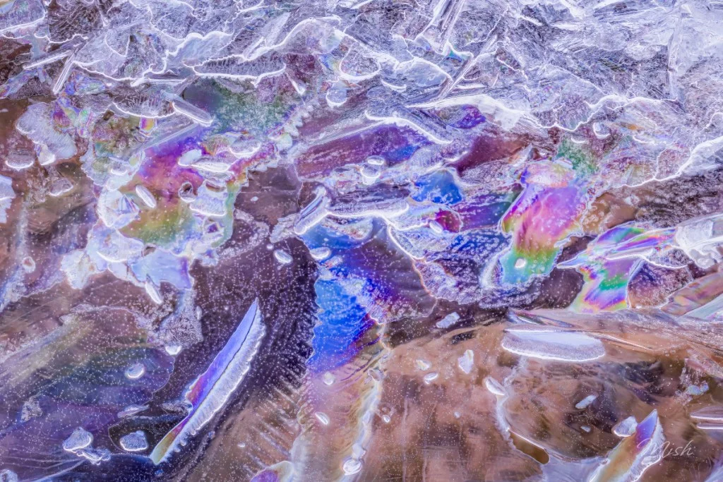 Close-up of colorful ice with iridescent patterns and textures.
