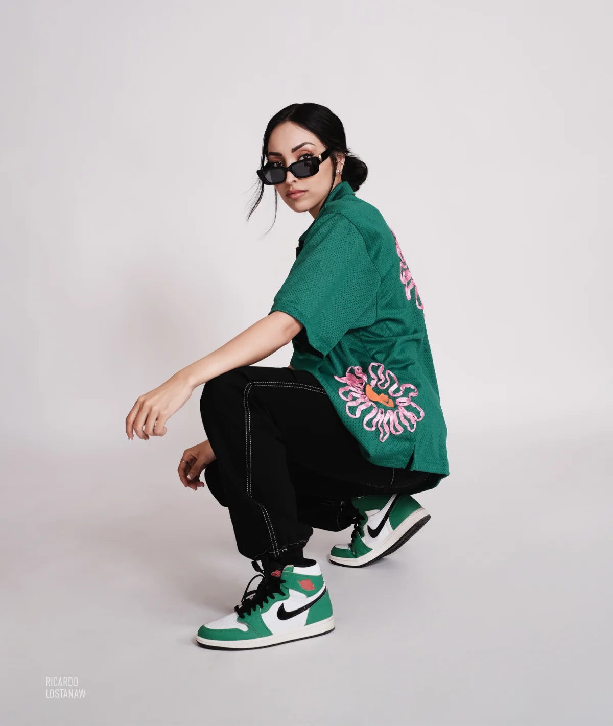 Model crouching in a green mesh jersey and green high-top sneakers on white seamless